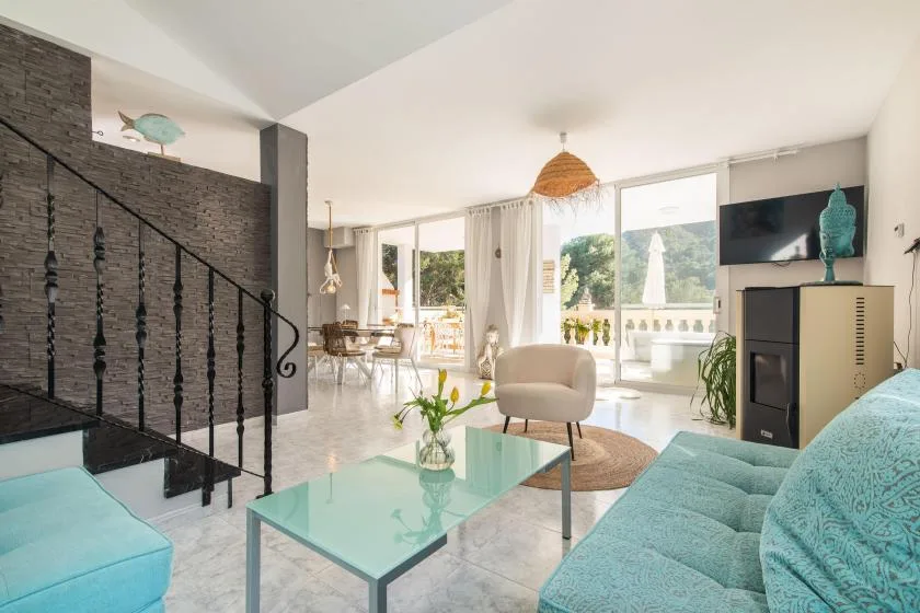 A bright living room with seating, a glass coffee table, and large windows.