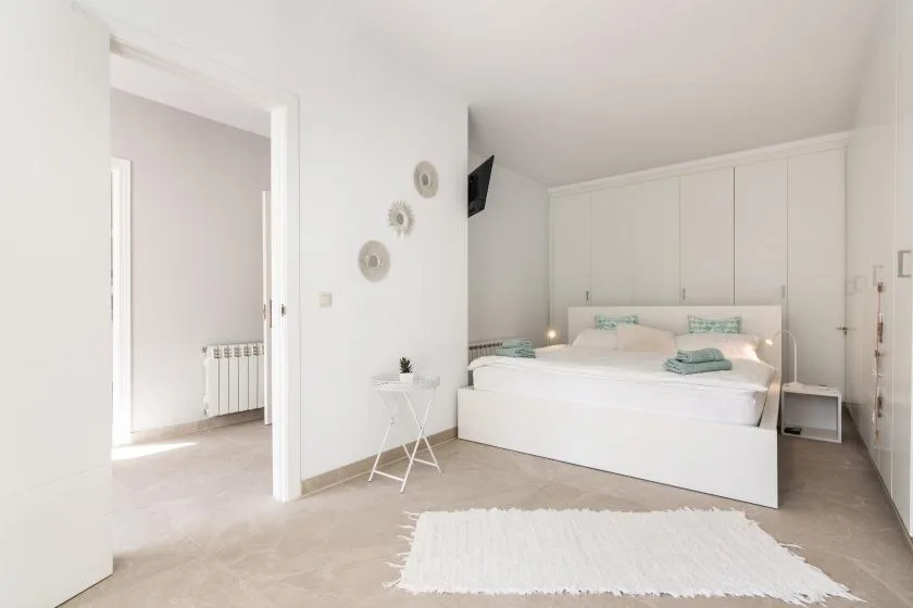 A bright bedroom with a bed, white cabinetry, and a small rug.