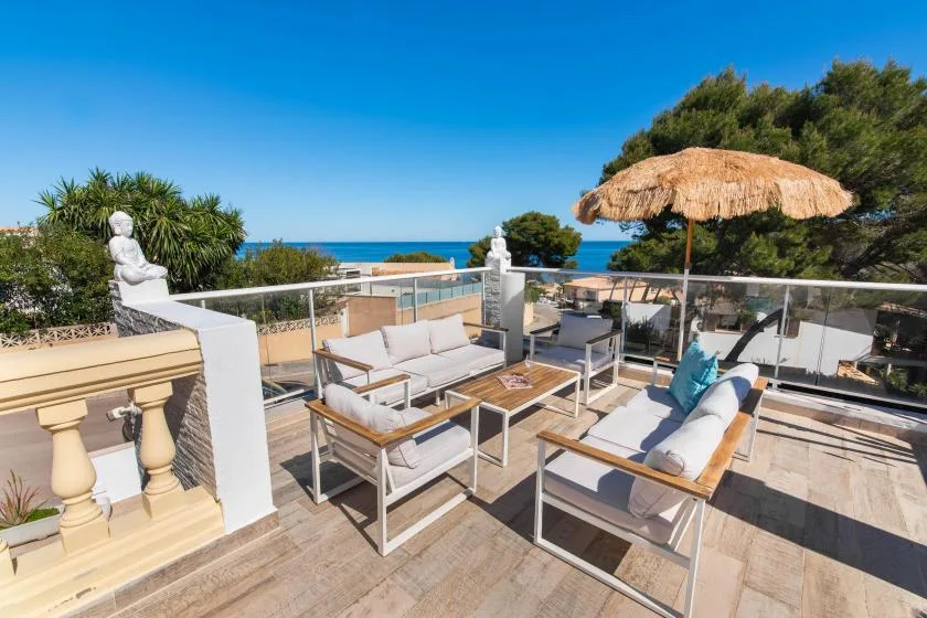 An outdoor terrace with cushioned seating and a thatched sun umbrella overlooks the sea.