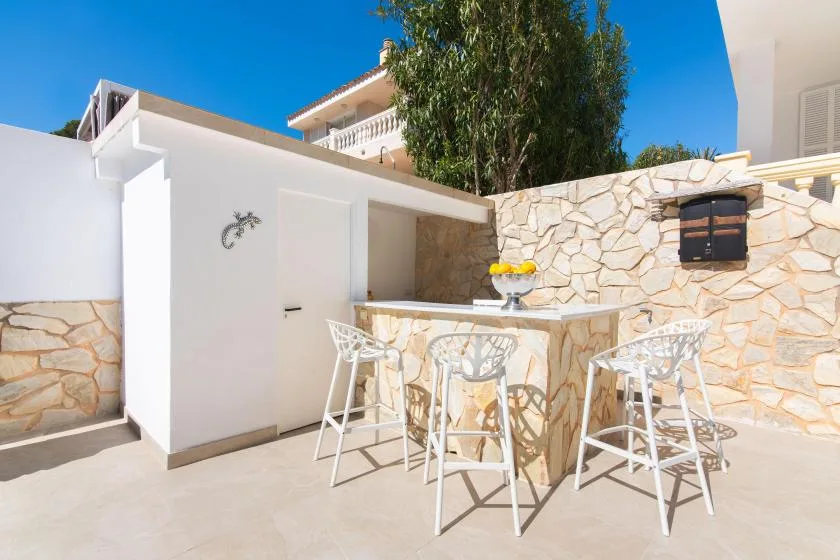 An outdoor patio has a stone bar counter and white seating.