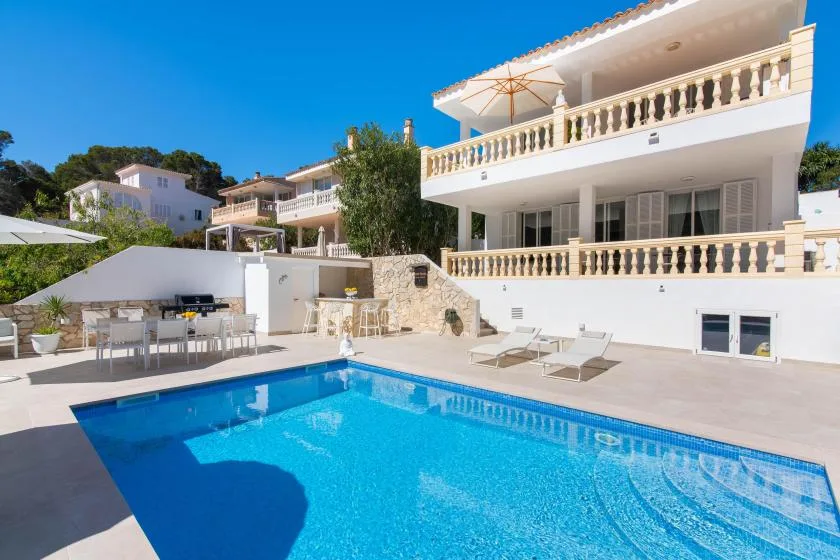 An outdoor swimming pool sits beside a white building with balconies and patio seating.