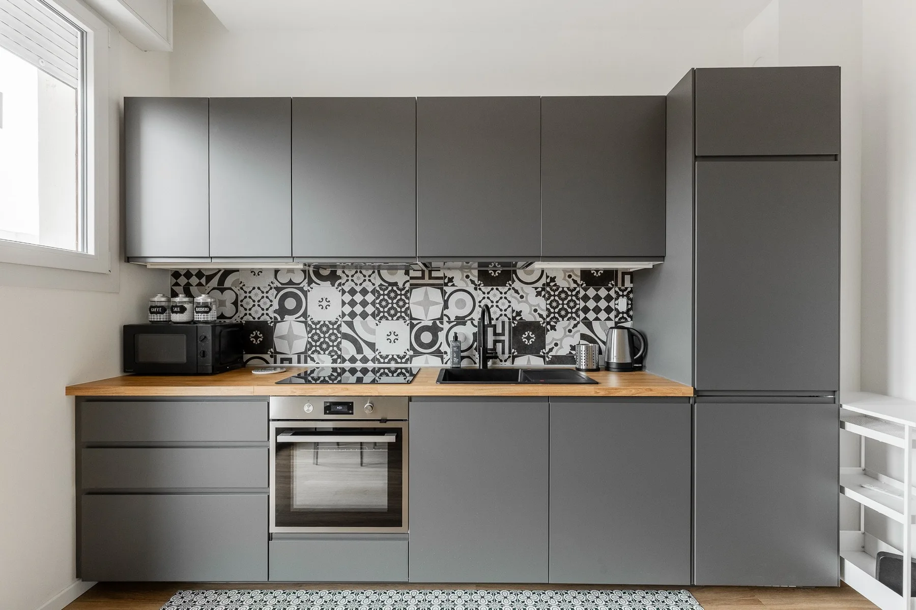 Una cocina moderna con gabinetes grises, electrodomésticos de acero inoxidable y salpicadero estampado.