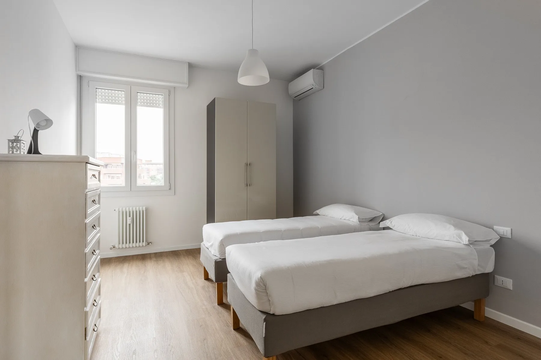 A bright bedroom with two single beds, a wardrobe, and a window.