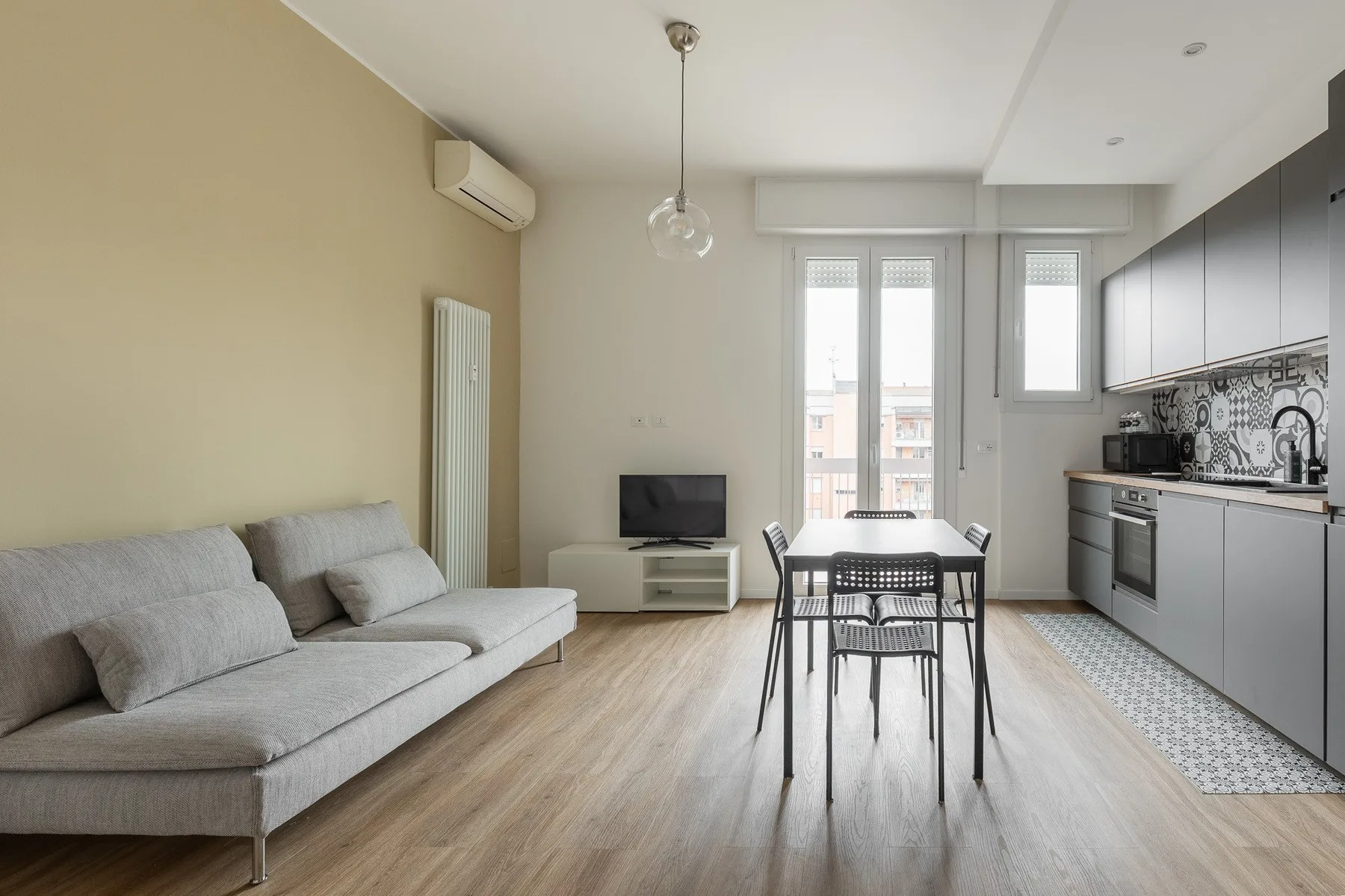A bright living and dining area with a sofa, table, and adjoining kitchen.
