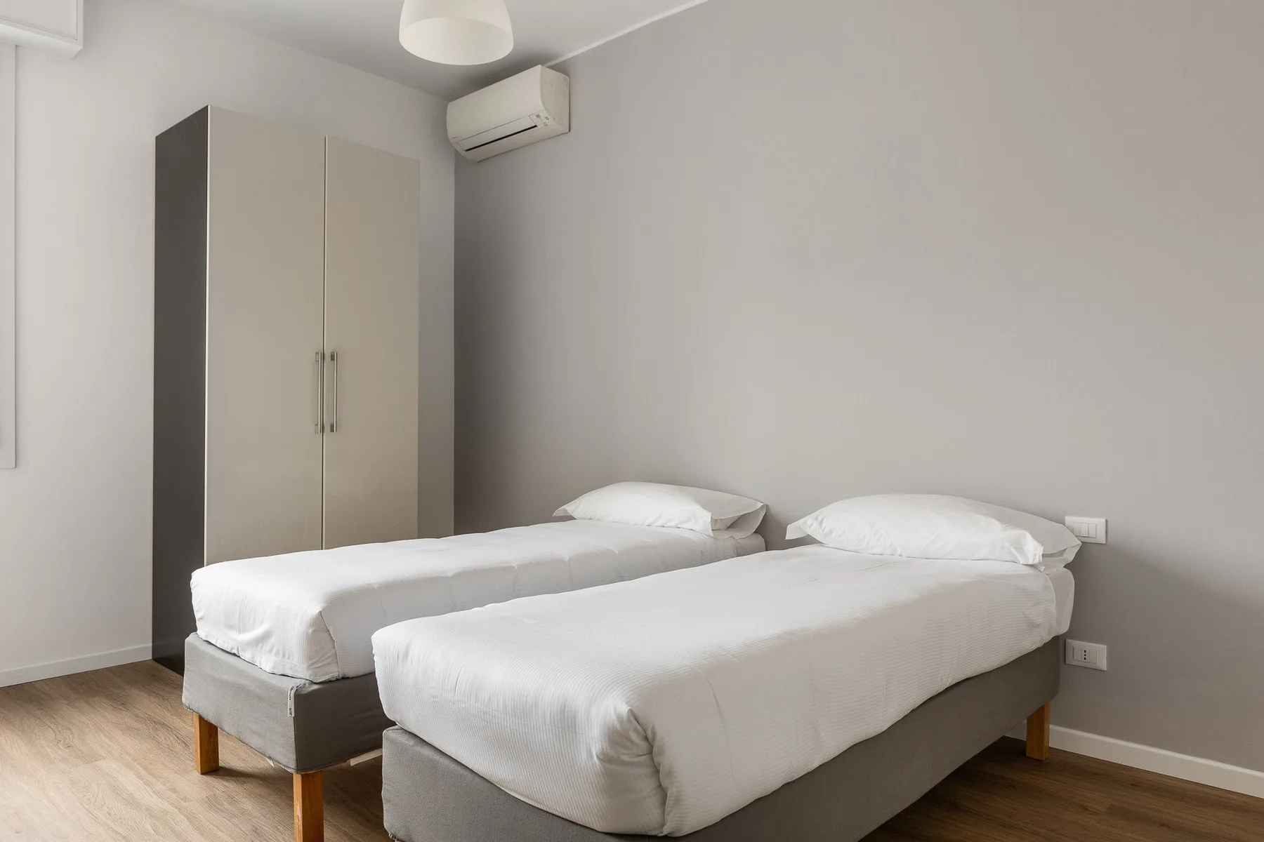 Un dormitorio con dos camas, ropa de cama blanca y un armario.