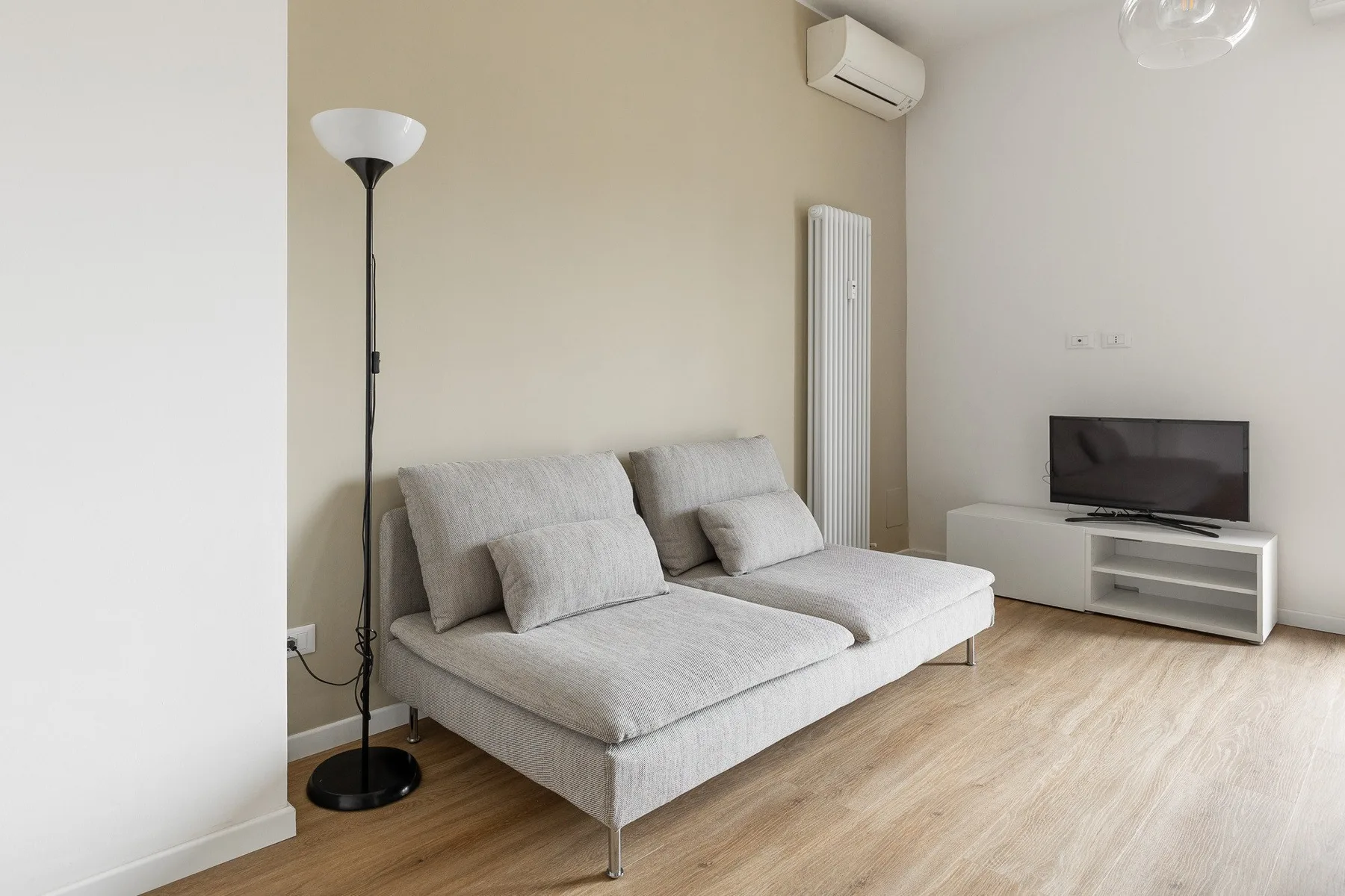 Una sala luminosa con un sofá seccional gris y un televisor.