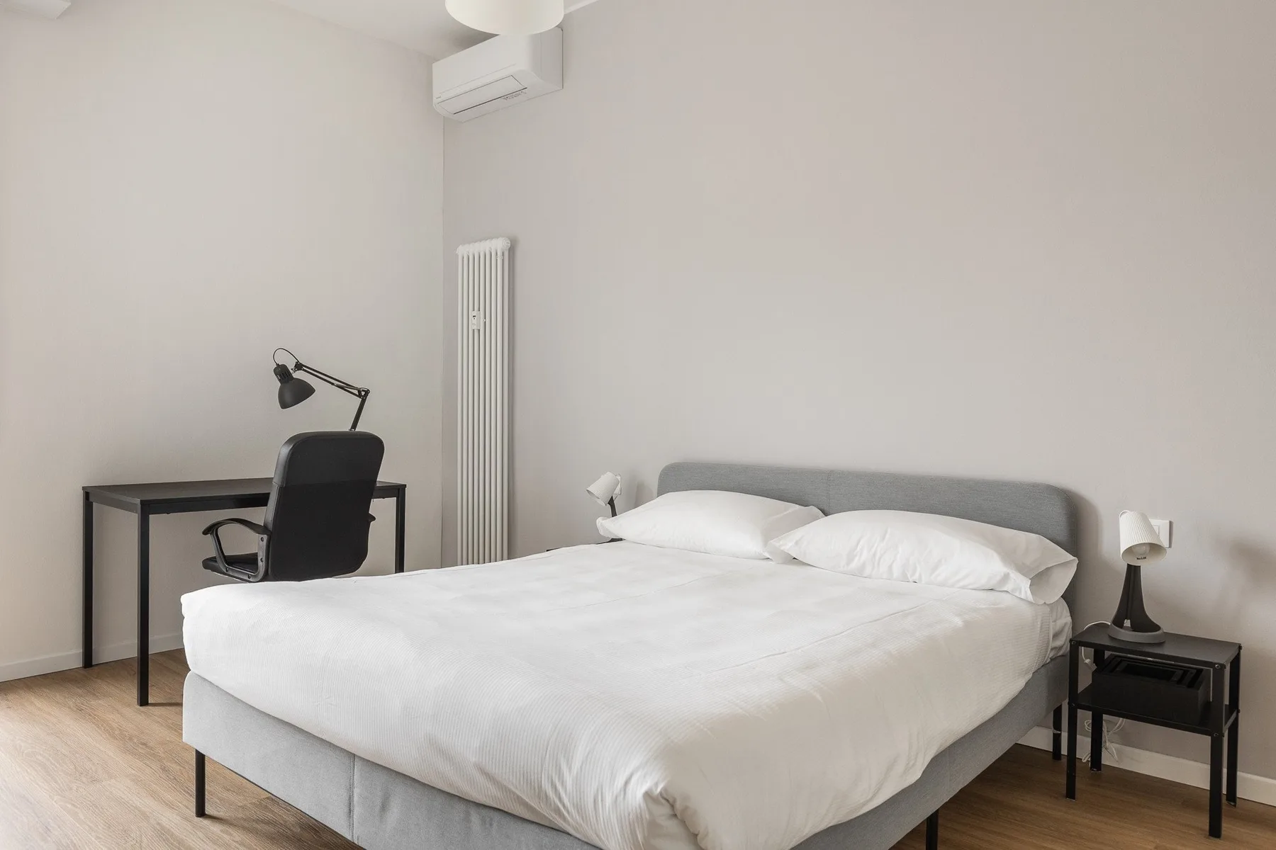 Un dormitorio luminoso con una cama, un escritorio y una mesita de noche.