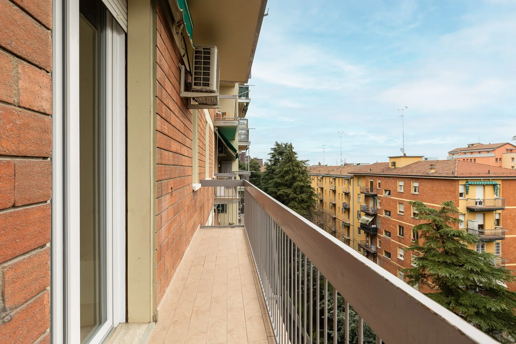 Un balcón estrecho da a edificios de apartamentos cercanos y árboles.