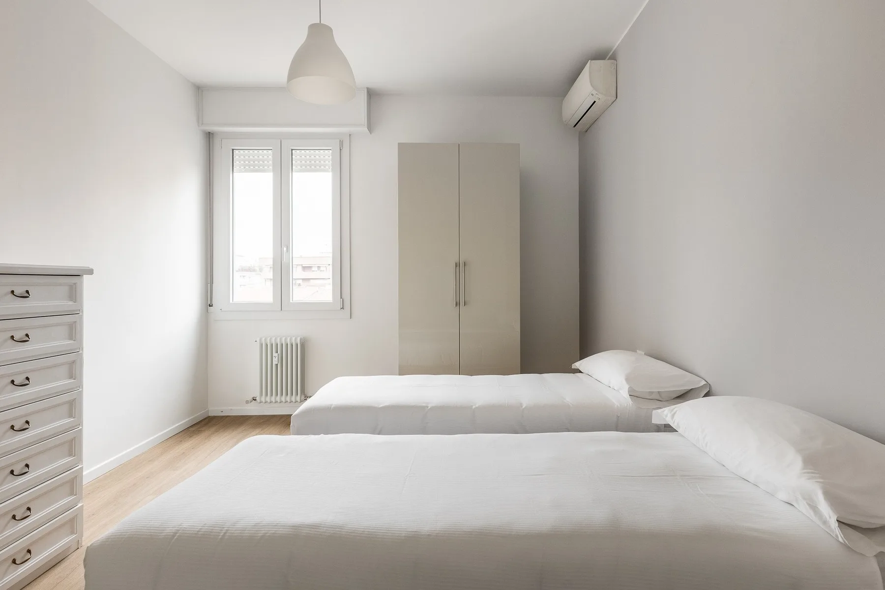 Un dormitorio luminoso con dos camas, un armario y una ventana.