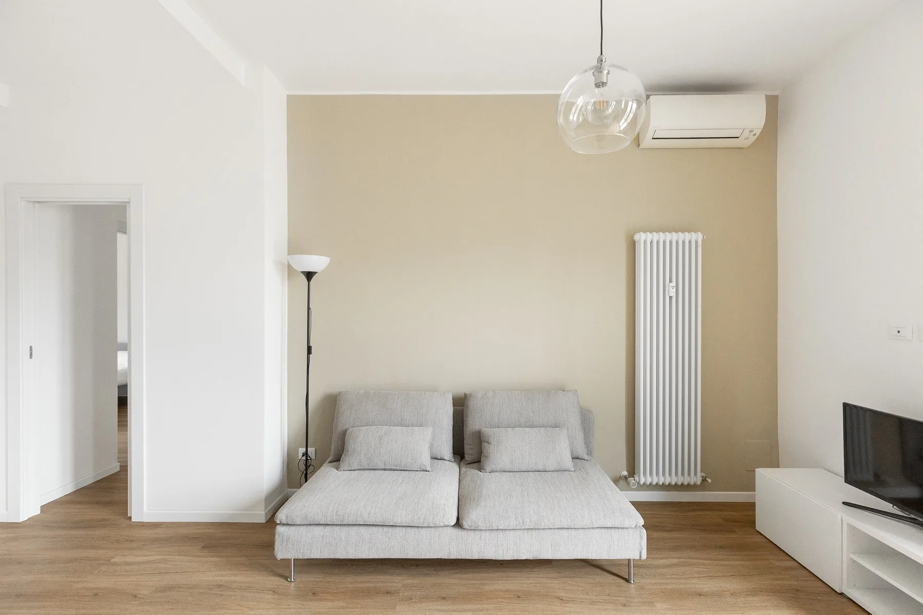 A bright bedroom with a low bed, floor lamp, and television.