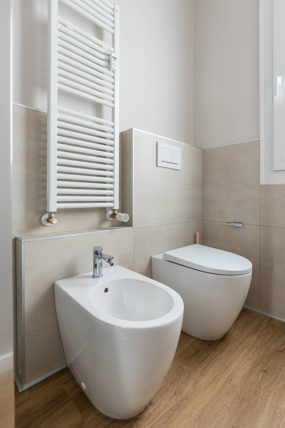 Un baño luminoso con bidé e inodoro bajo un toallero calefactable.