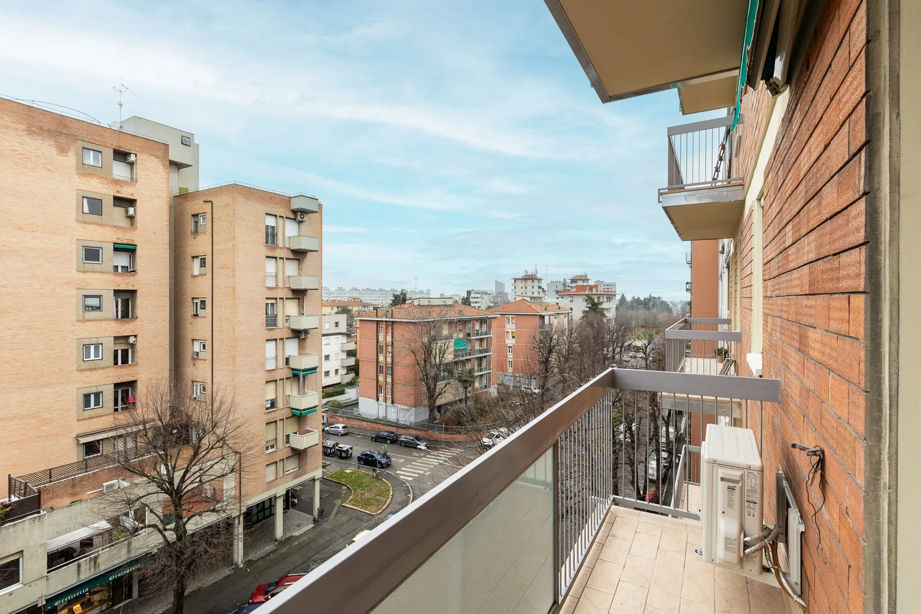 Un balcón da a edificios de apartamentos vecinos y una calle arbolada.