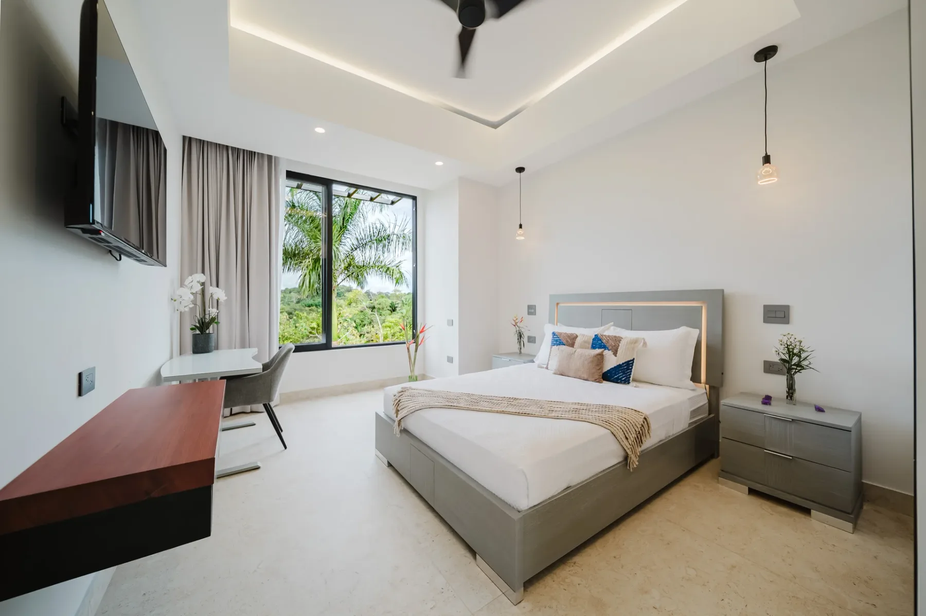 Casa Ama · 11. A bright bedroom features a contemporary bed with integrated backlighting, a ceiling fan, and a large window presenting a verdant tropical view.
