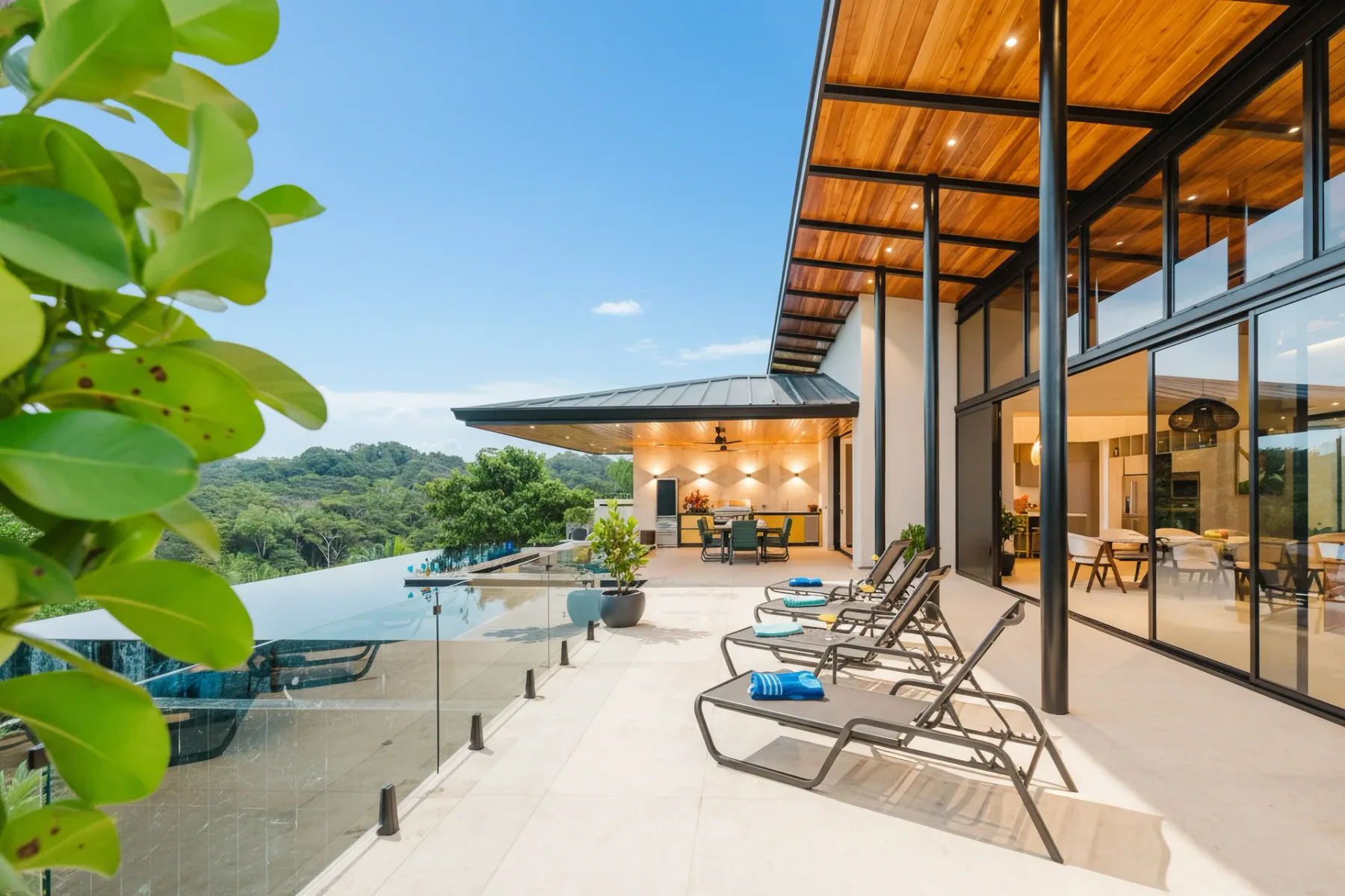 Casa Ama · 29. An open, sunlit terrace features an infinity pool with glass railings, an outdoor dining area, and unobstructed views of the jungle, connecting to the villa's modern interior through tall glass doors.