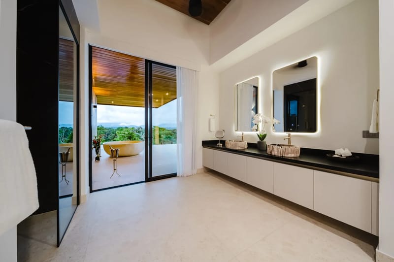 Casa Ama · 48. The spacious bathroom features a double vanity and opens through large glass doors to a private outdoor terrace with a freestanding tub overlooking a lush jungle landscape.