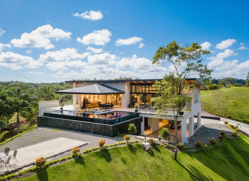 Casa Ama · 23. A modern multi-level villa with an infinity pool and expansive glass walls integrates with the surrounding tropical landscape under an open sky.