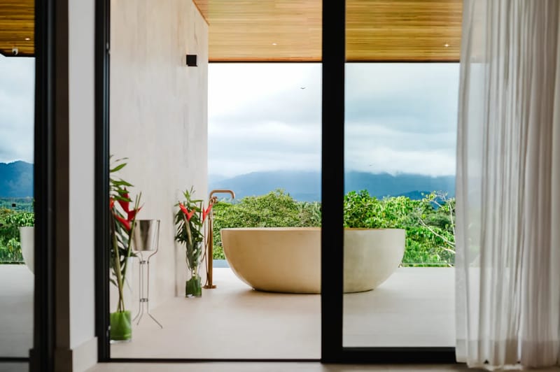 Casa Ama · 42. An open-air bathing area features a freestanding tub on a terrace, overlooking forested mountains and the sky through large glass doors.
