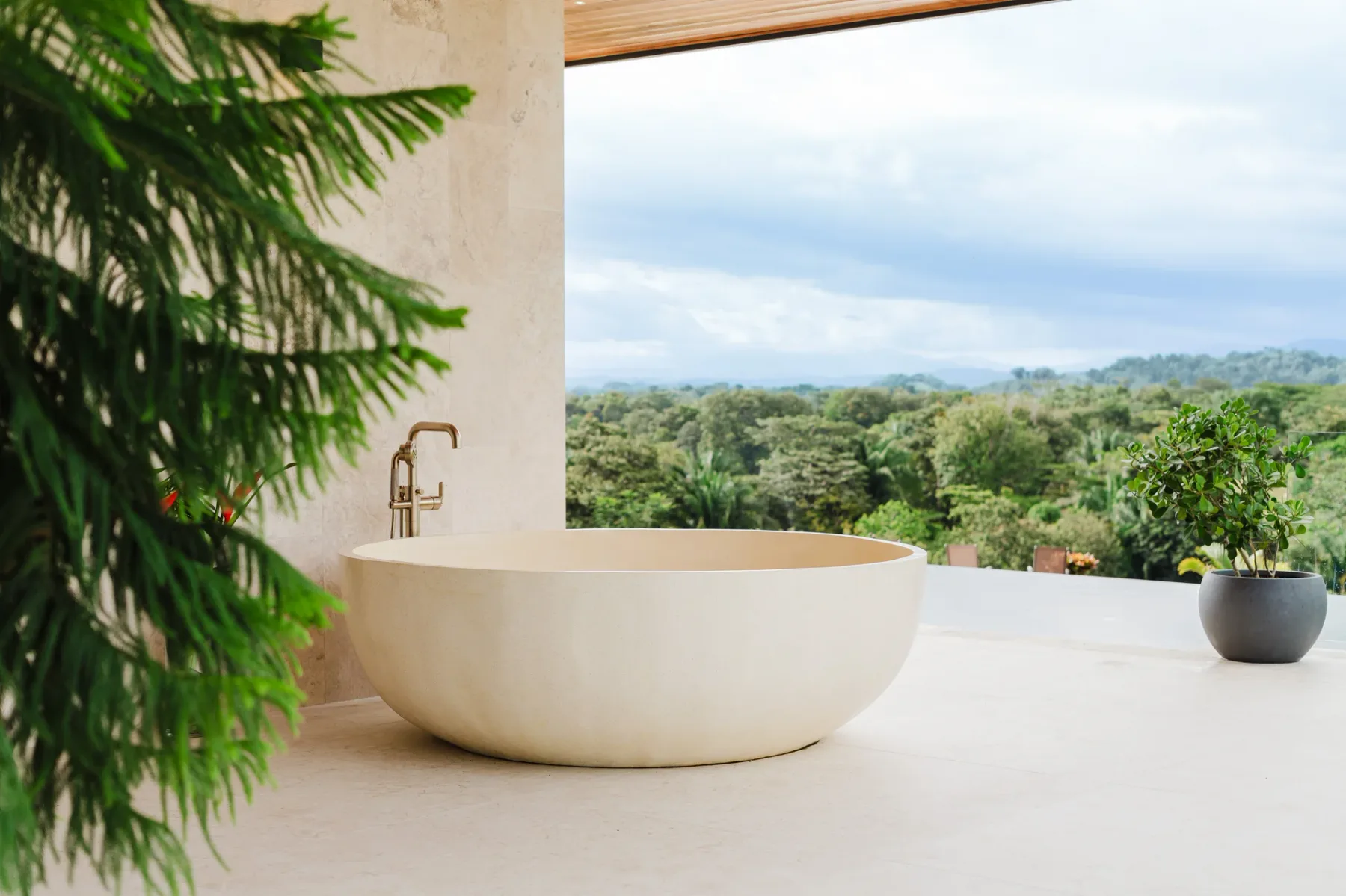 Casa Ama · 10. A large freestanding tub with a brass faucet is positioned next to an open wall looking out to a sprawling jungle and mountain view.