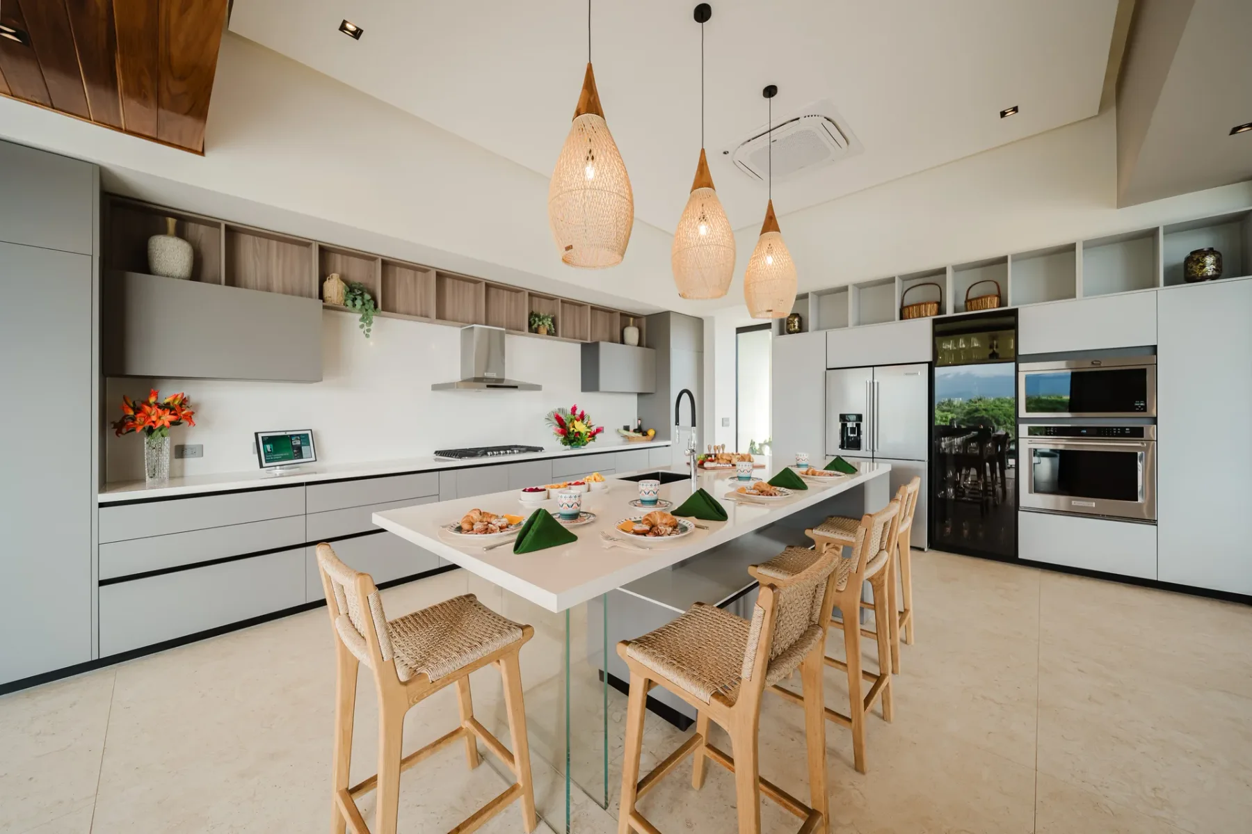 Casa Ama · 31. A bright, contemporary kitchen features light grey cabinetry, a large island with bar seating, integrated appliances, and views to the outdoors.