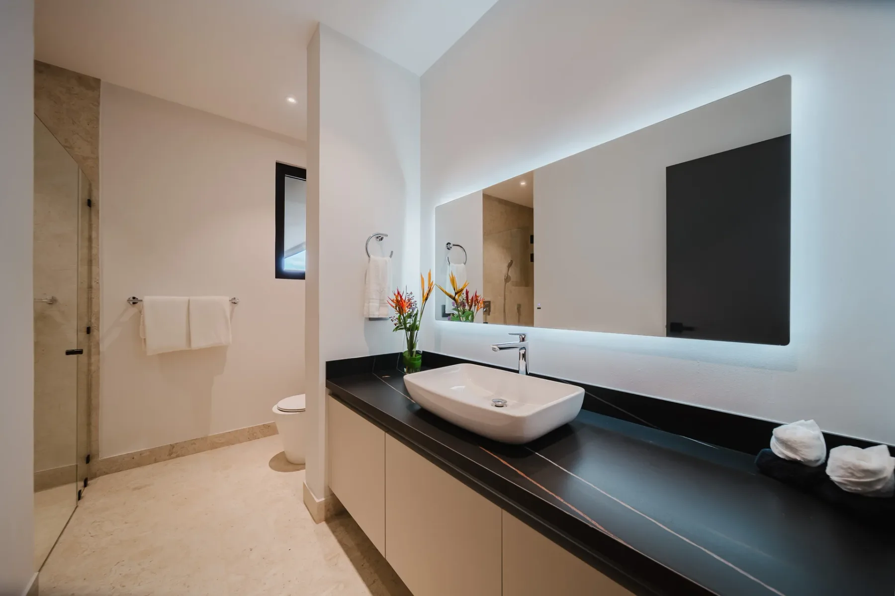 Casa Ama · 46. A bright, modern bathroom features a sleek vanity with a vessel sink, a large backlit mirror, and a walk-in shower with a glass enclosure.
