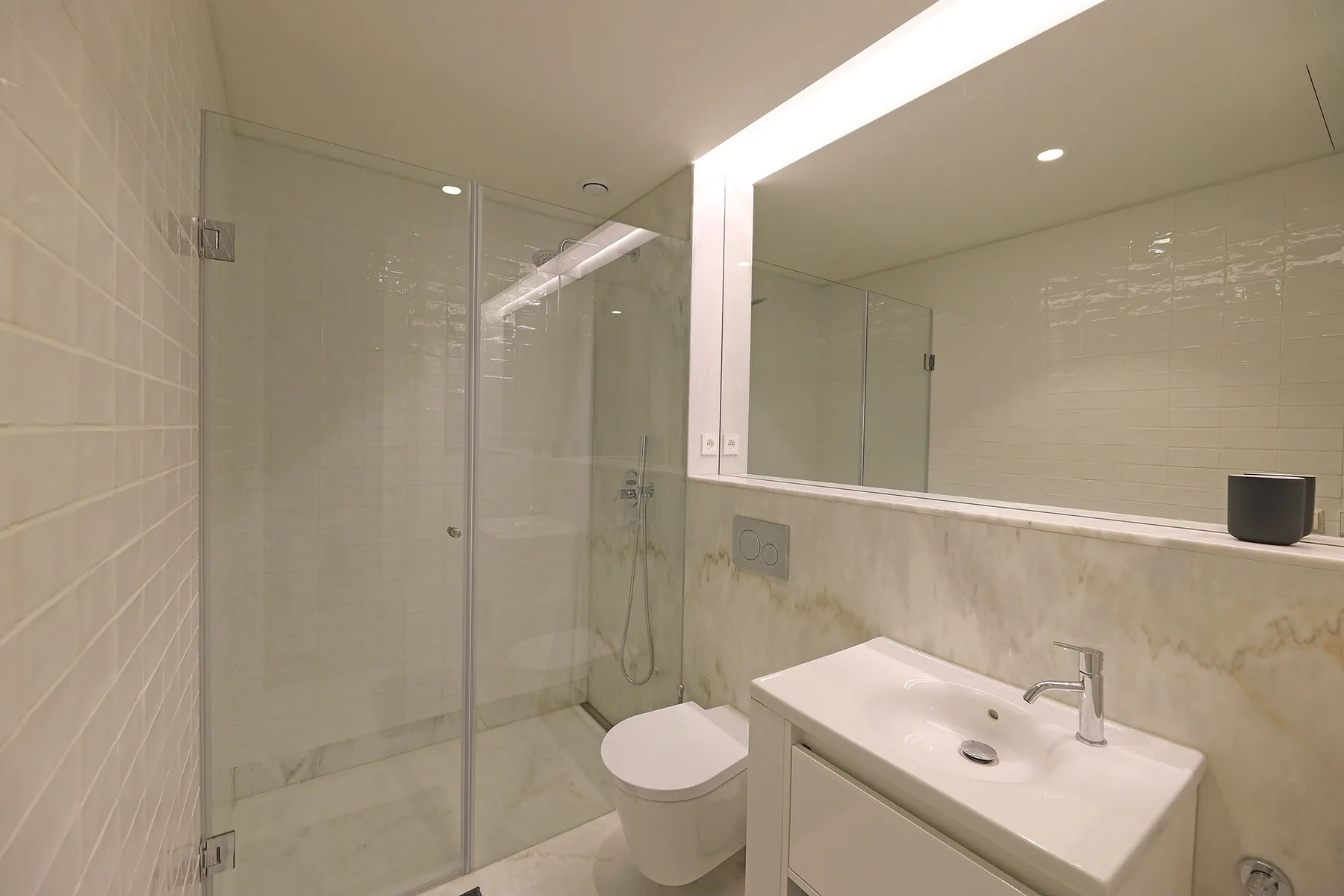 Un baño con ducha de vidrio, inodoro y lavabo bajo un espejo grande.