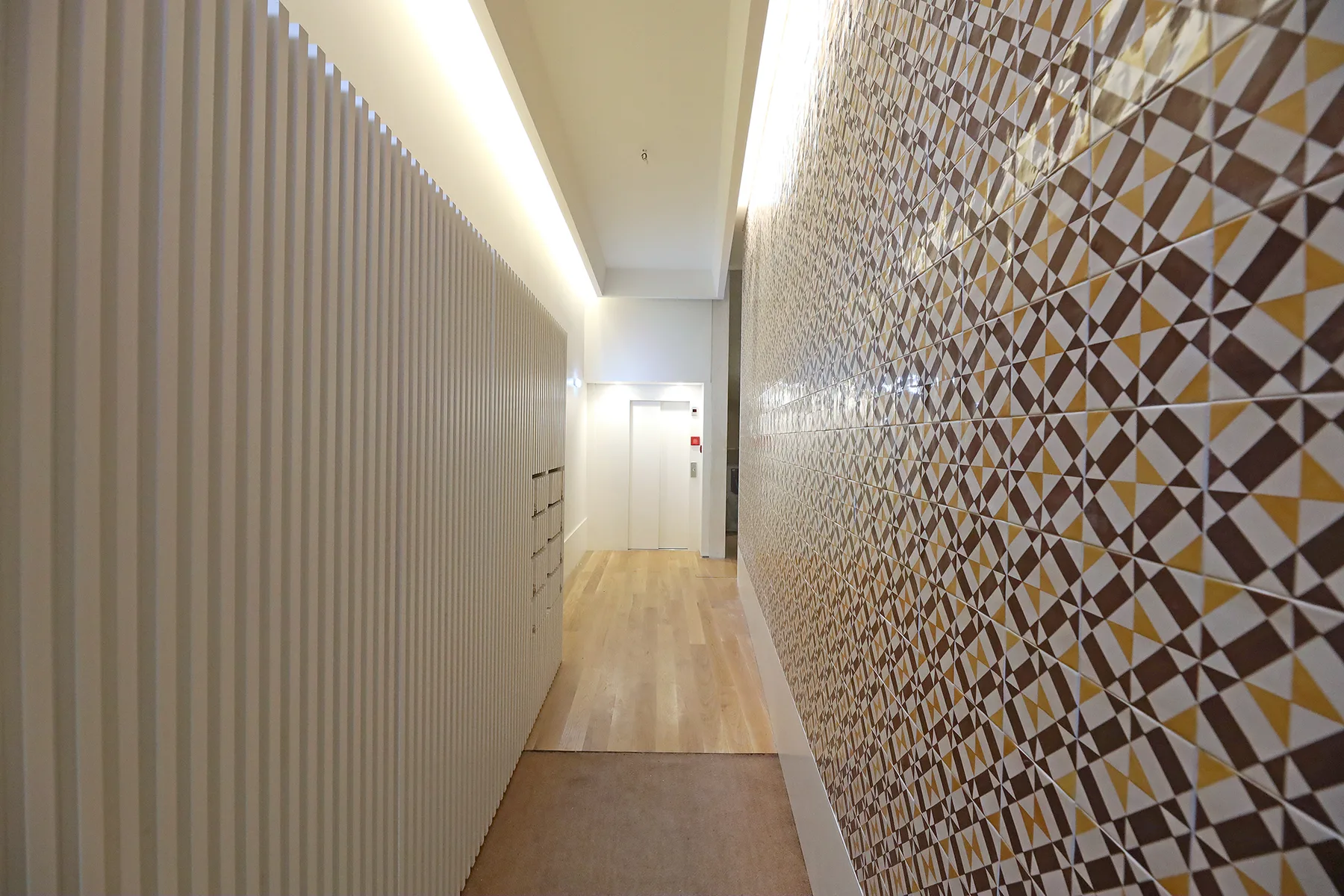 Un pasillo estrecho con suelo de madera y una pared con motivos geométricos.