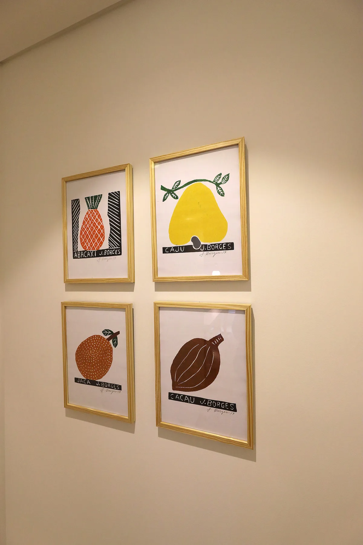 Cuatro láminas de frutas enmarcadas cuelgan de una pared clara.