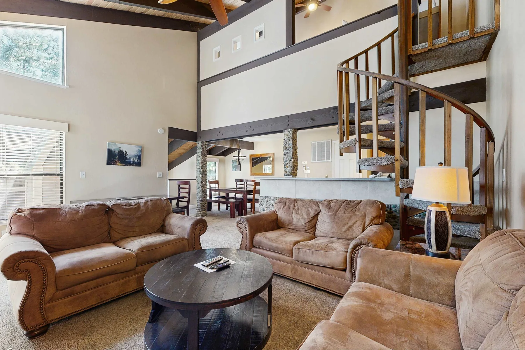 A living room with brown seating, a coffee table, and a spiral staircase.