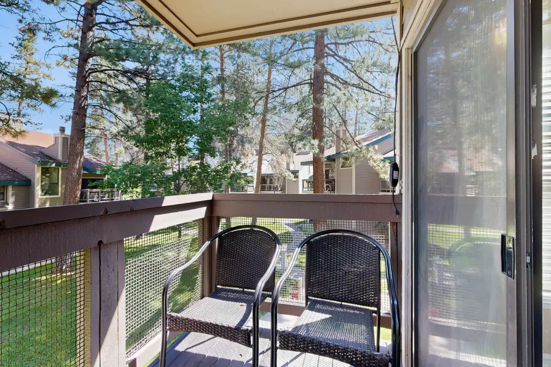 A small deck with two chairs overlooks trees and nearby buildings.