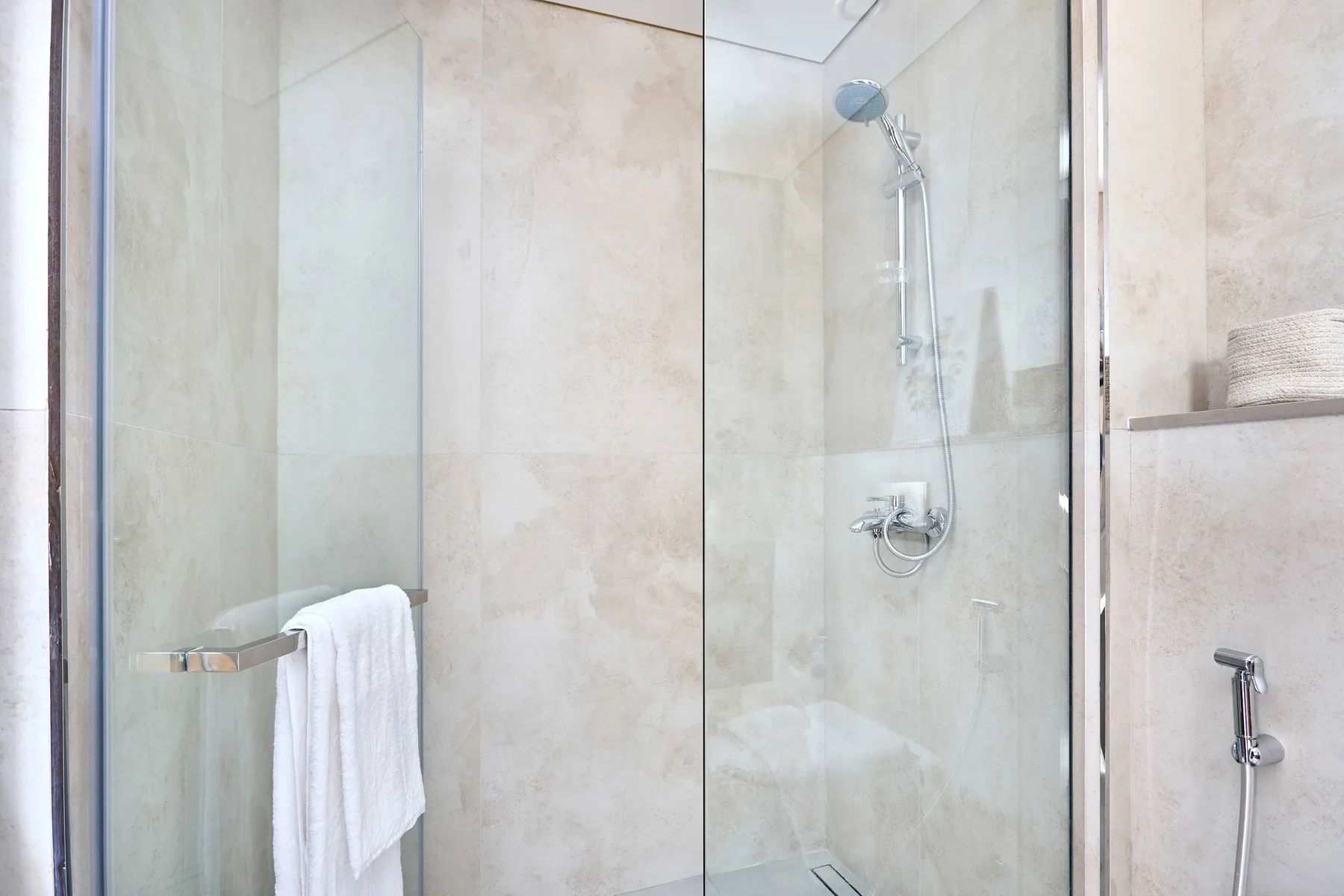 Una ducha de baño con azulejos, paneles de vidrio y una toalla colgada cerca.