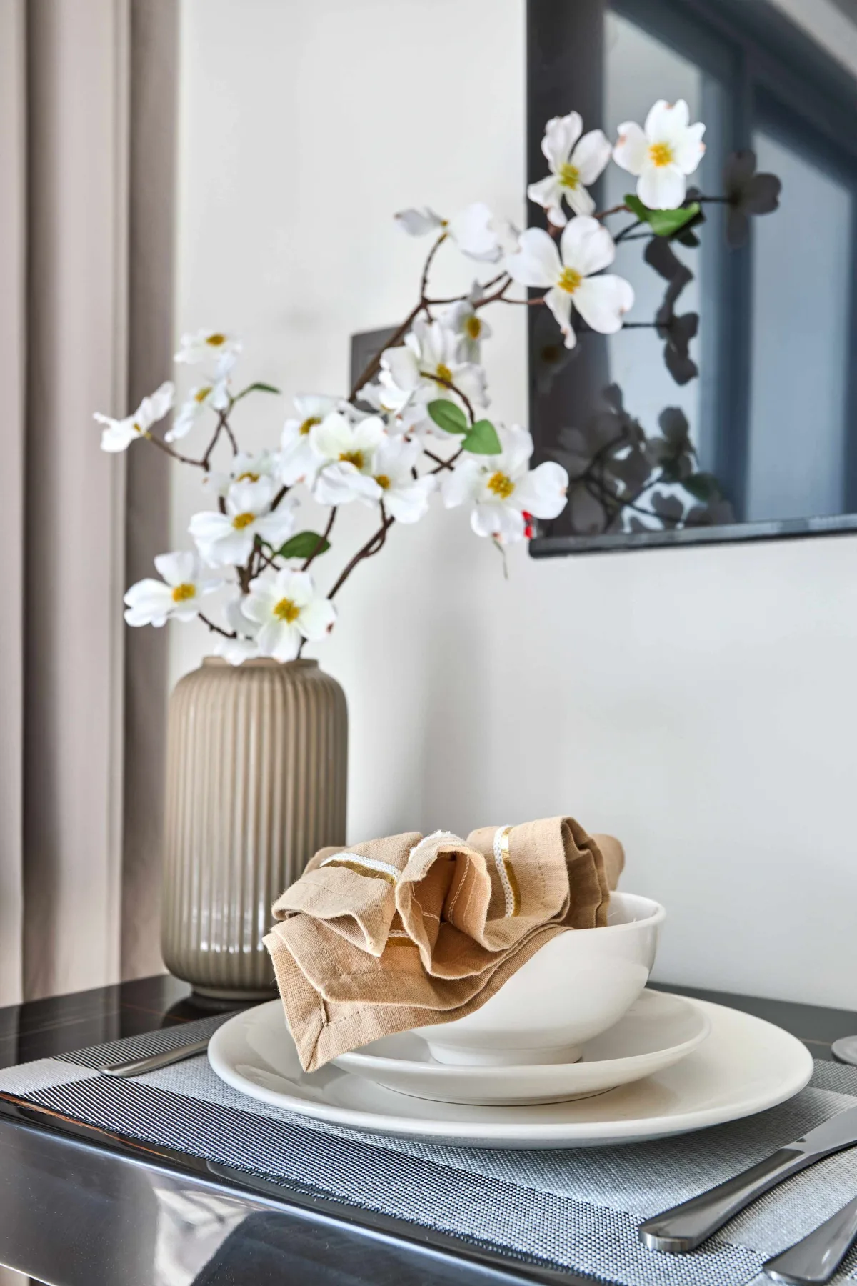 Una mesa está preparada con un cuenco blanco, una servilleta doblada y ramas con flores.