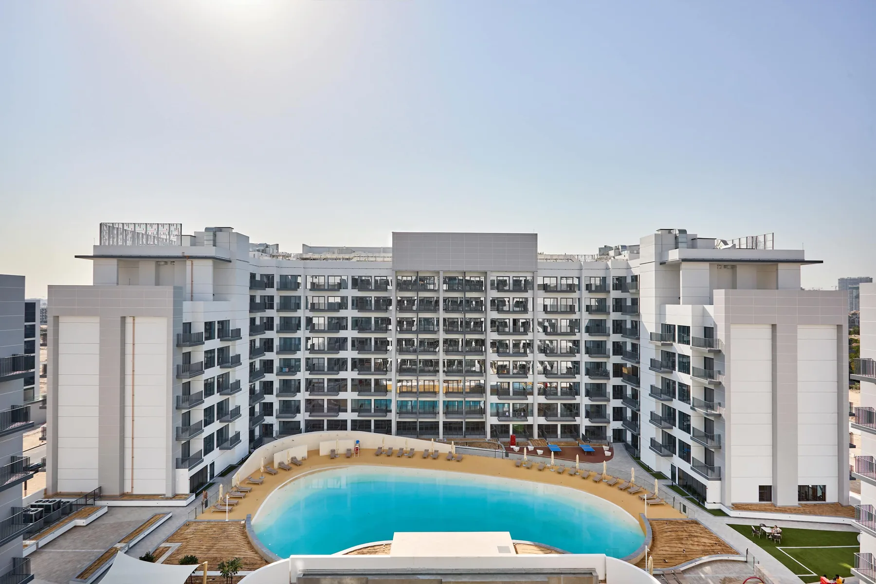 Un gran edificio hotelero da al patio con una piscina curva.