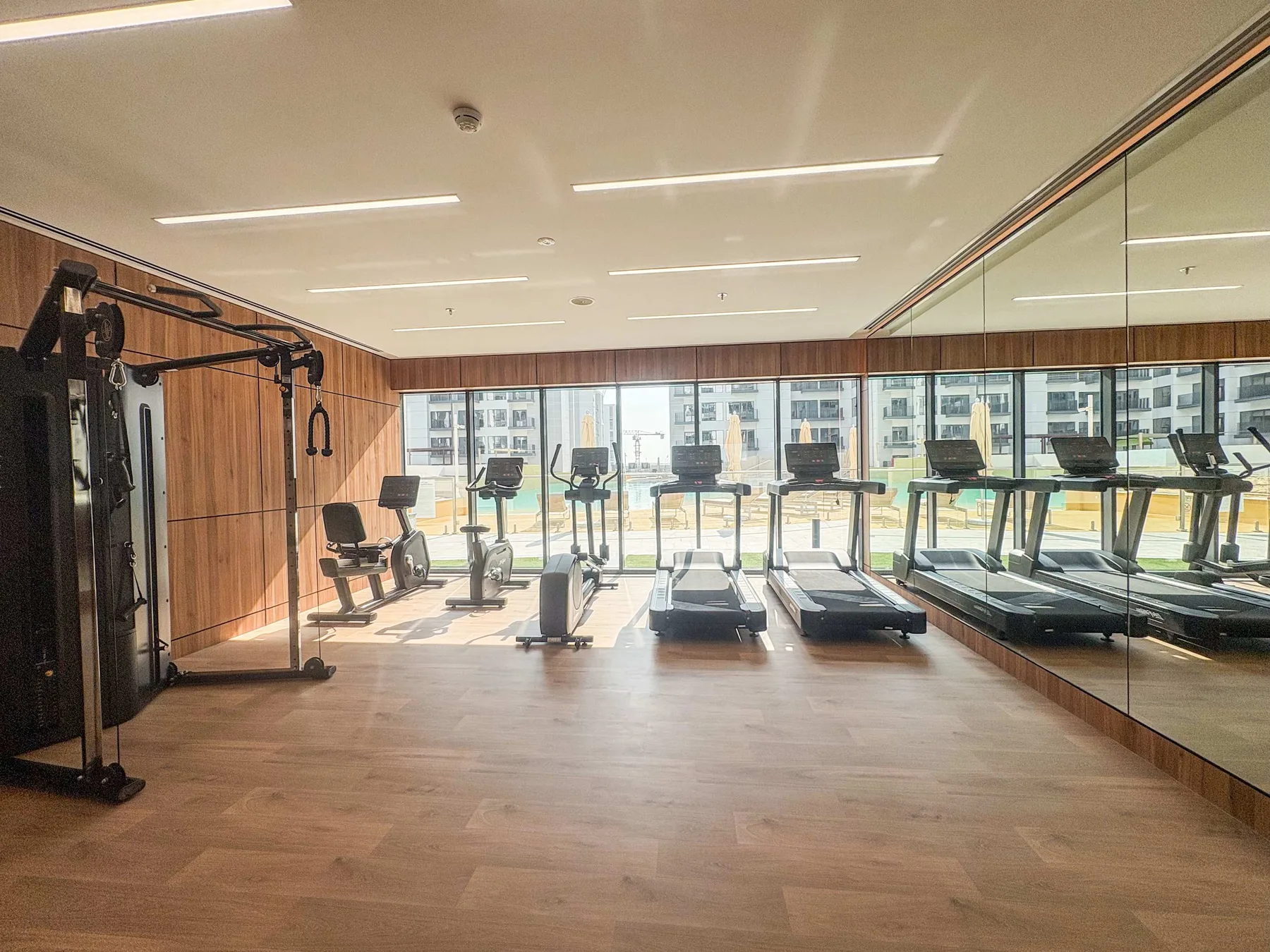 Un gimnasio con máquinas de ejercicio y cintas de correr junto a paredes con espejos.