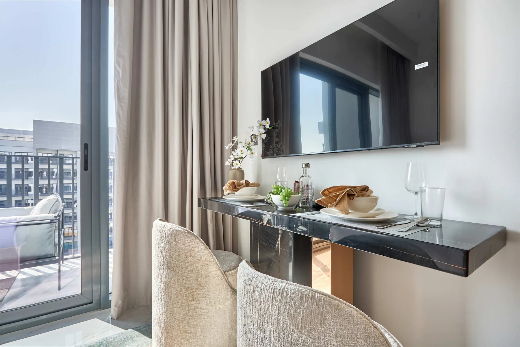 Comedor con un televisor montado en la pared y una puerta de vidrio que da a un balcón.
