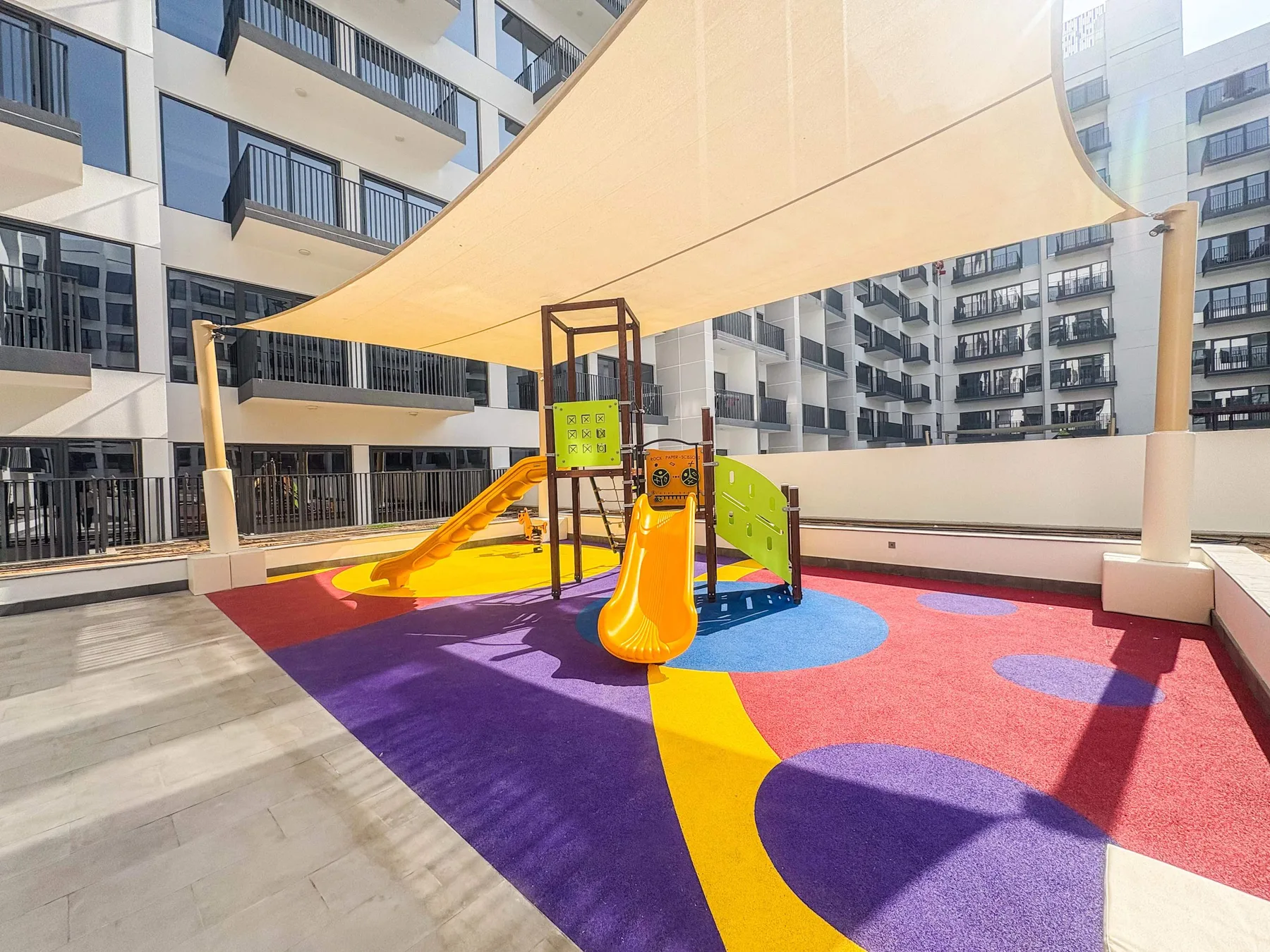 Un colorido parque infantil en la azotea está bajo una gran lona de sombra.