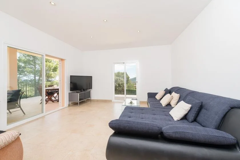 Una sala luminosa con un sofá seccional oscuro y puertas corredizas de vidrio.