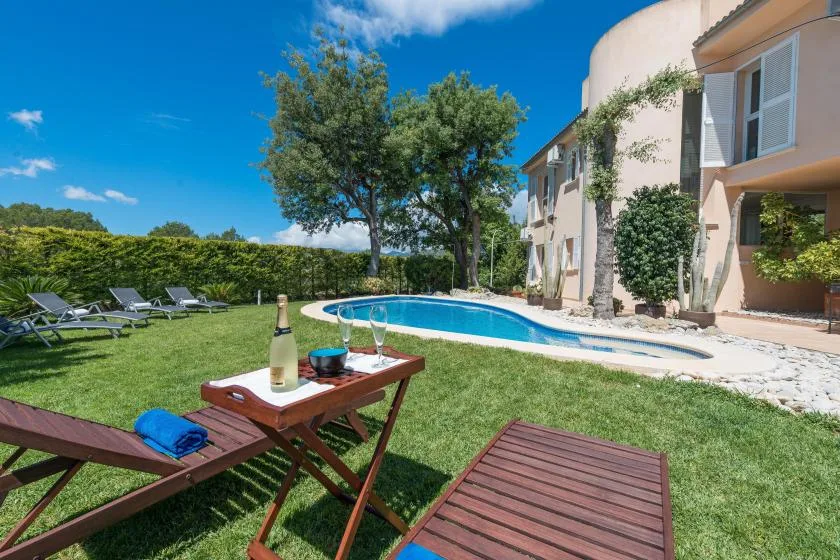 Una piscina junto a un jardín con césped, tumbonas y una mesa.