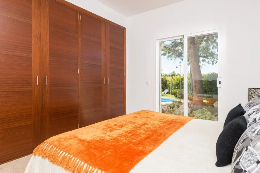 Dormitorio con una colcha naranja y puertas corredizas de vidrio con vistas a la vegetación.