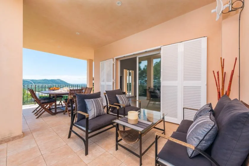 Un patio cubierto tiene asientos acolchados y una mesa de comedor con vistas al paisaje.
