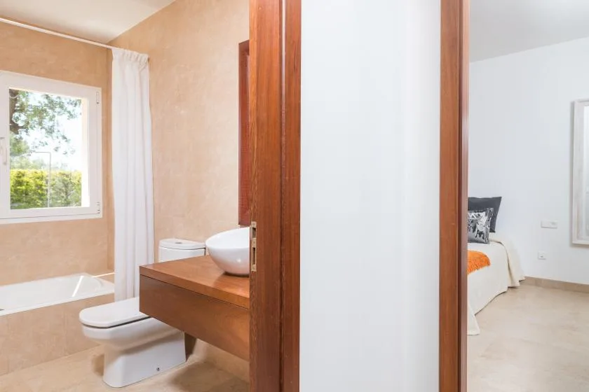 Un baño con bañera, inodoro y tocador se abre a un dormitorio.