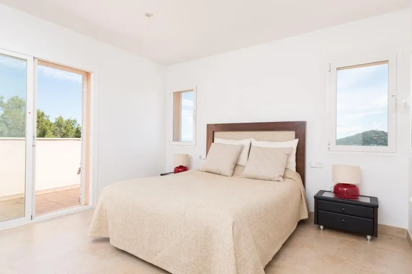 Un dormitorio luminoso con una cama tendida y ventanas con vistas al paisaje.