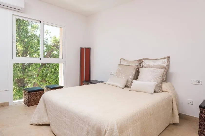 Un dormitorio luminoso con una cama grande junto a una ventana con vistas a la vegetación.