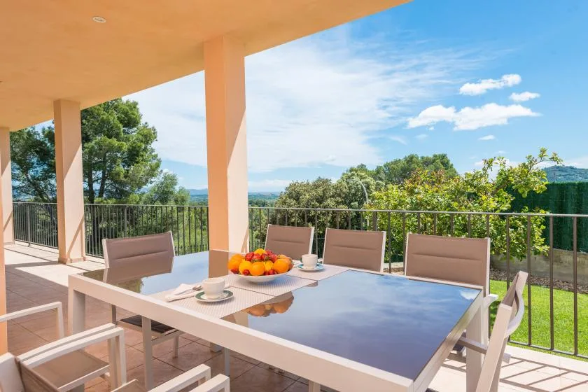 Una mesa de comedor y asientos en un patio dan a la vegetación bajo un cielo despejado.