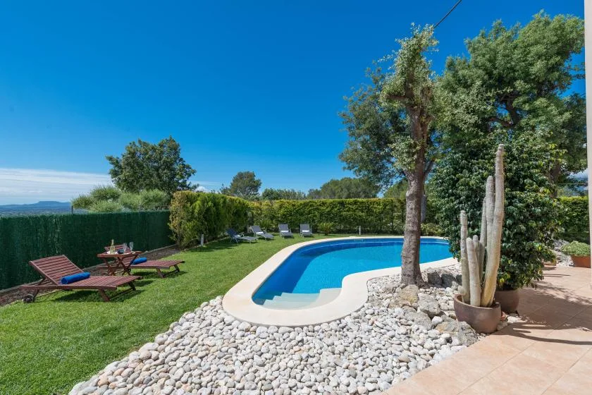 Una piscina al aire libre está junto a un césped y un jardín cuidado.