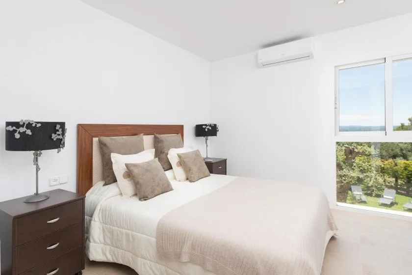 Un dormitorio luminoso con una cama bien tendida y ventanas grandes.