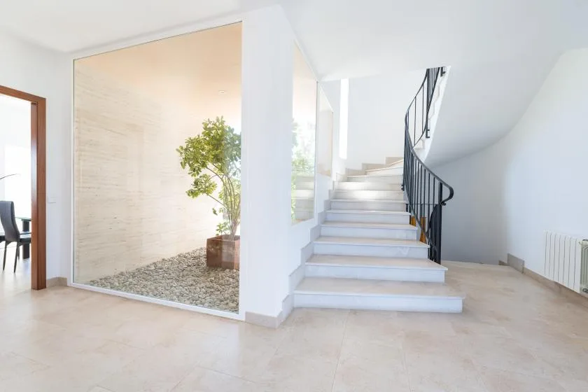 Un pasillo interior luminoso tiene una escalera junto a un pequeño jardín interior.