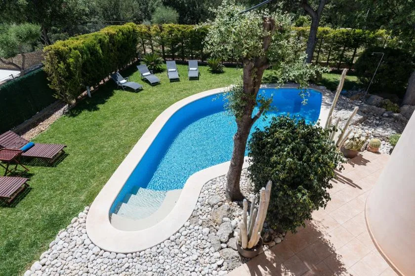 Una piscina curva está junto a un jardín con césped y árboles alrededor.