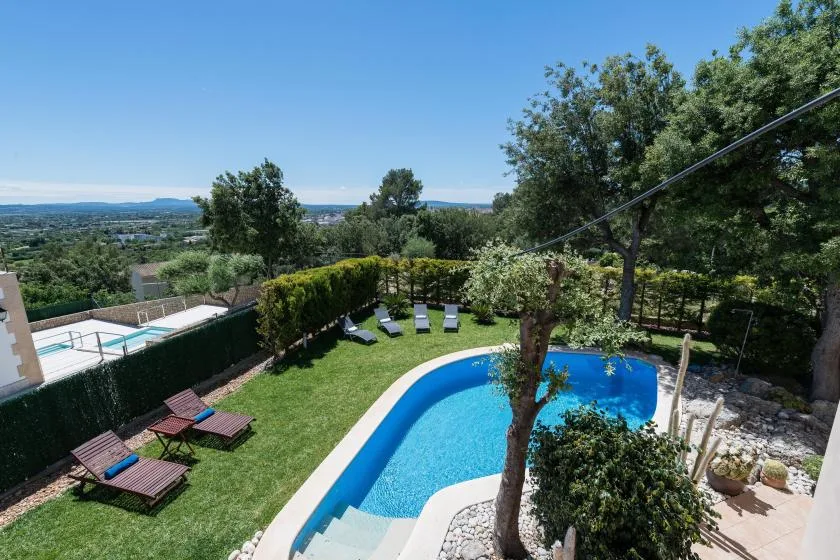 Un jardín trasero con una piscina curva y tumbonas ofrece vistas a un paisaje verde.