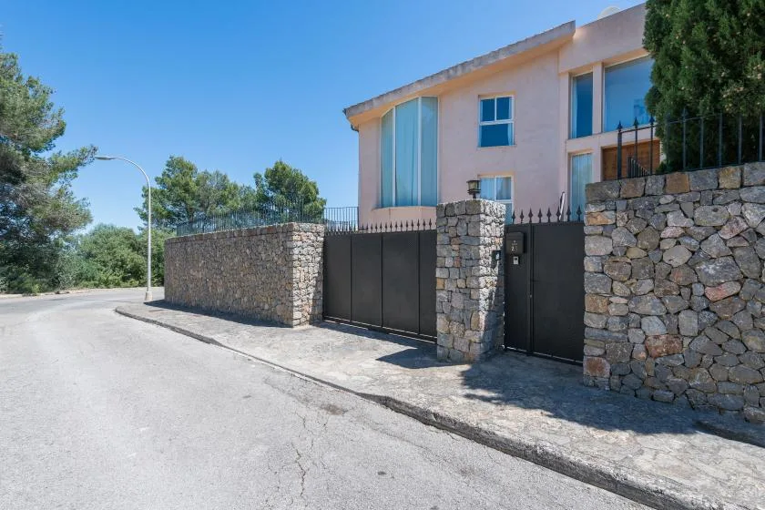 Una casa moderna se alza tras un portón oscuro y muros de piedra.