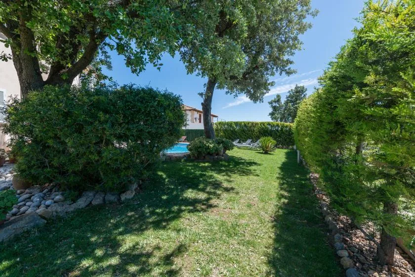 Un jardín ajardinado con árboles, setos y una vista parcial de una piscina.